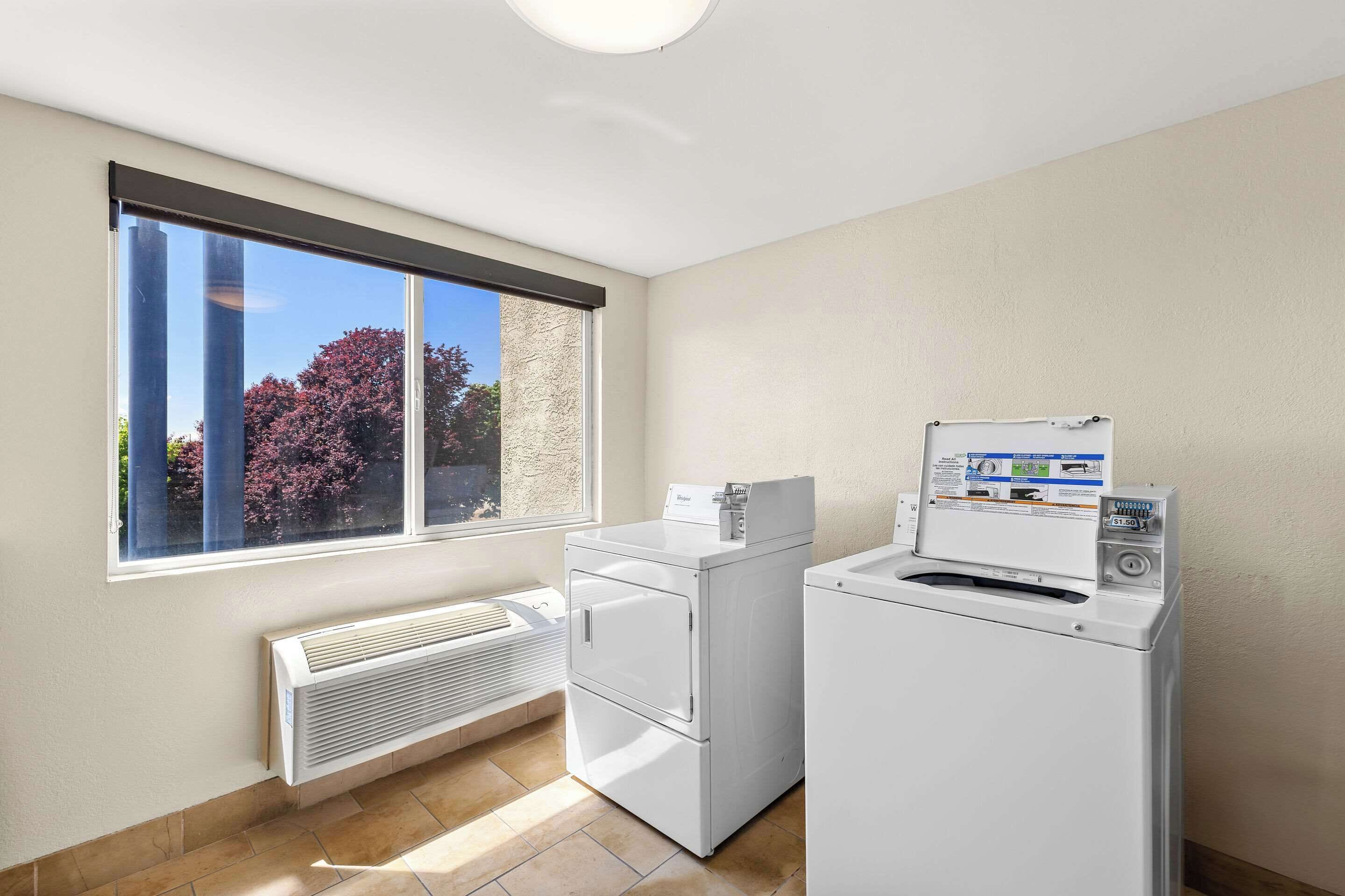A laundry room with a washer and dryer, a vent, and a window with blinds.