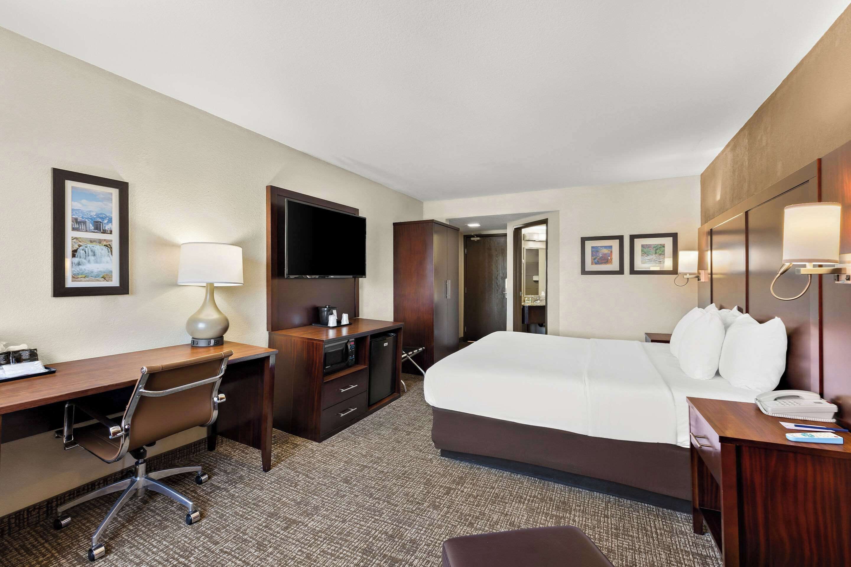 A hotel room with a large bed, a desk with a chair, a TV, and a wardrobe.