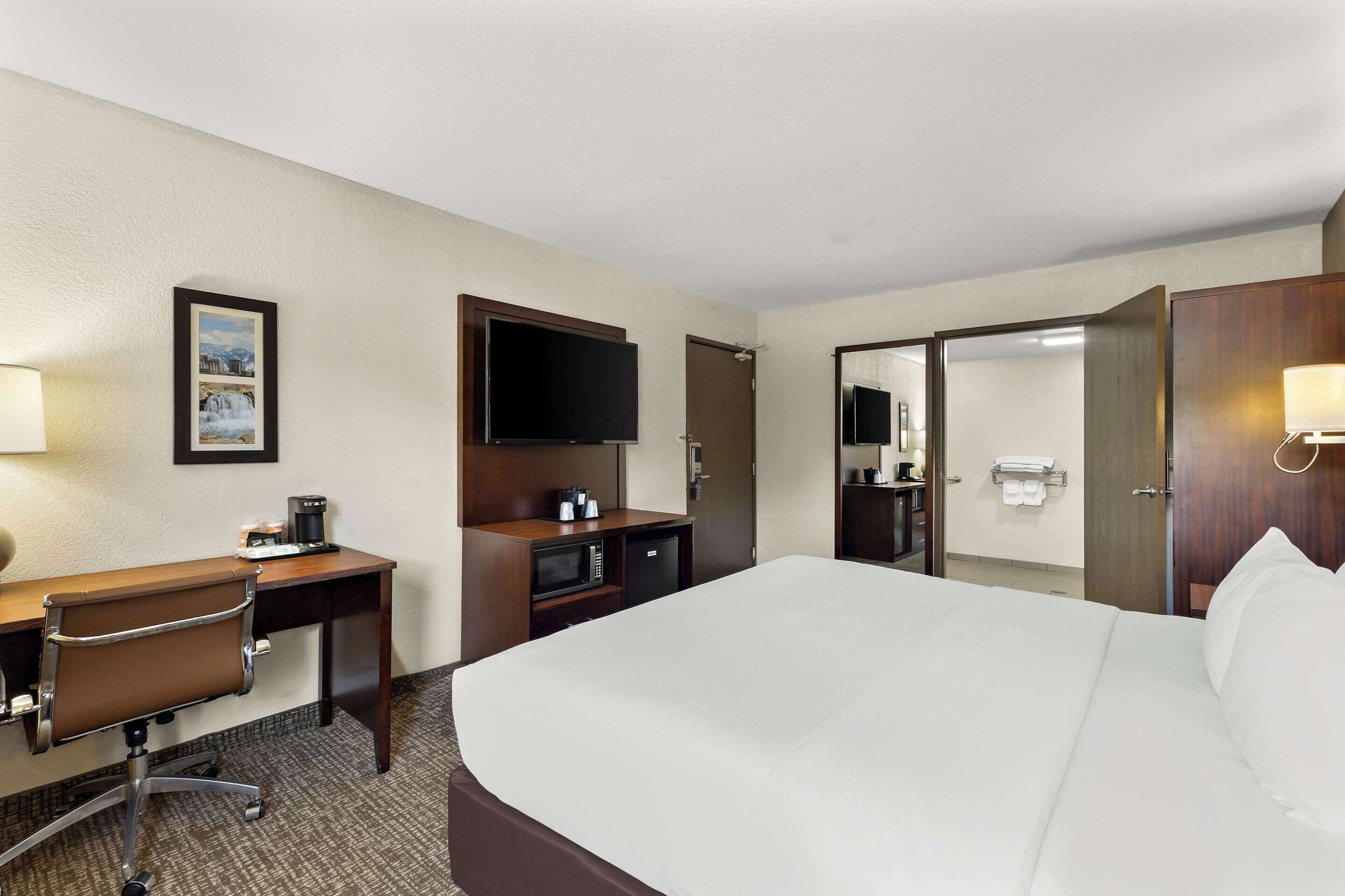A hotel room with a large bed, a desk with a chair, a television, a microwave, and a door leading to a bathroom.