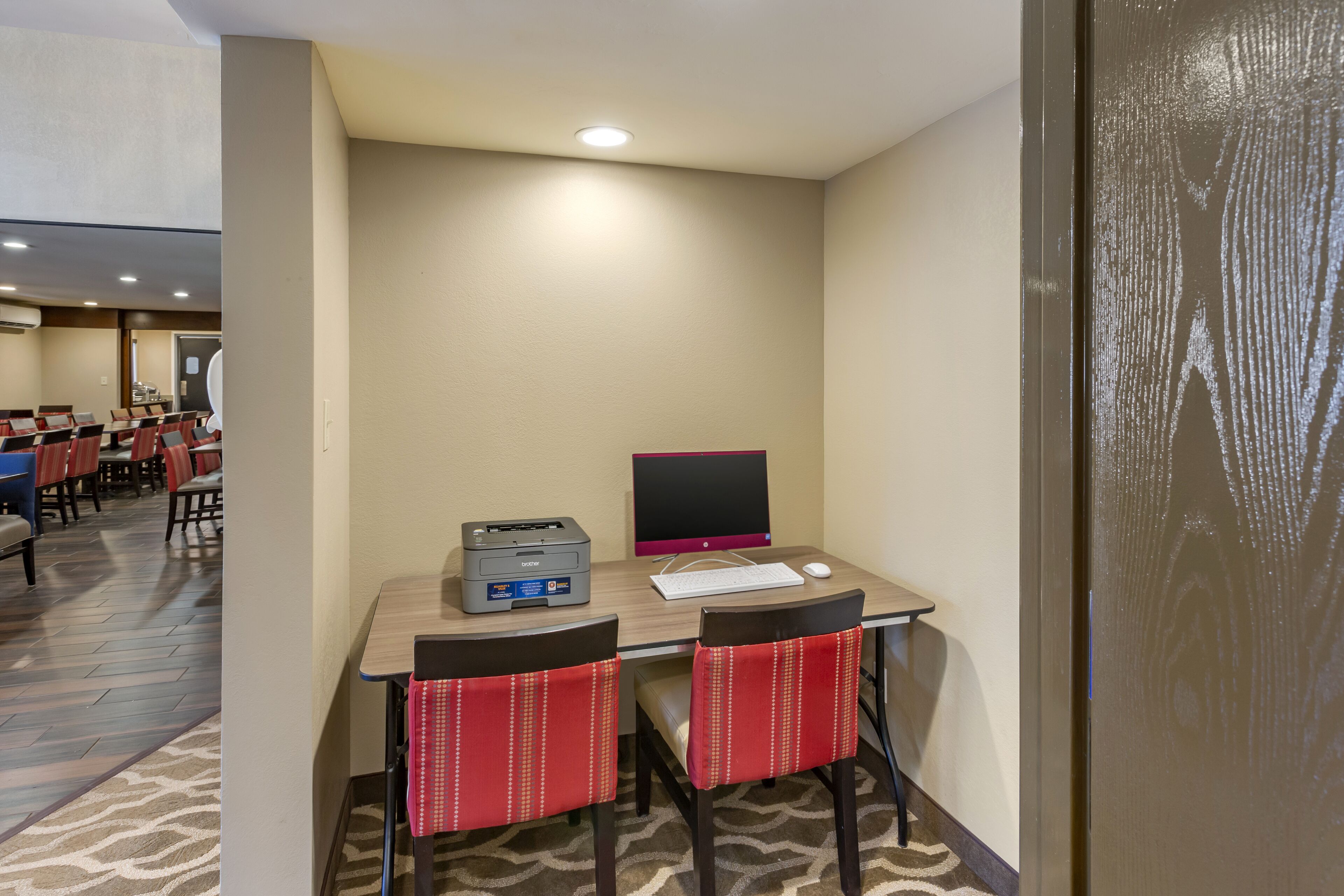 A hotel room with a desk, two chairs, a computer, and a printer.