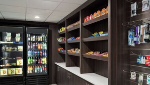 Zona de máquinas expendedoras con aperitivos y bebidas, y estantes con artículos de higiene personal.