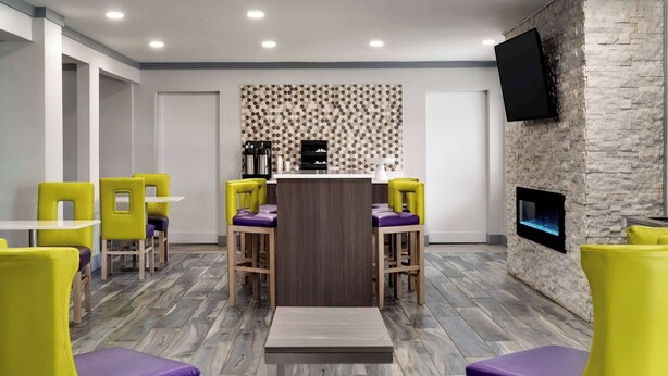 Un comedor moderno con sillas amarillas, una mesa central y una pared de piedra con un televisor montado.