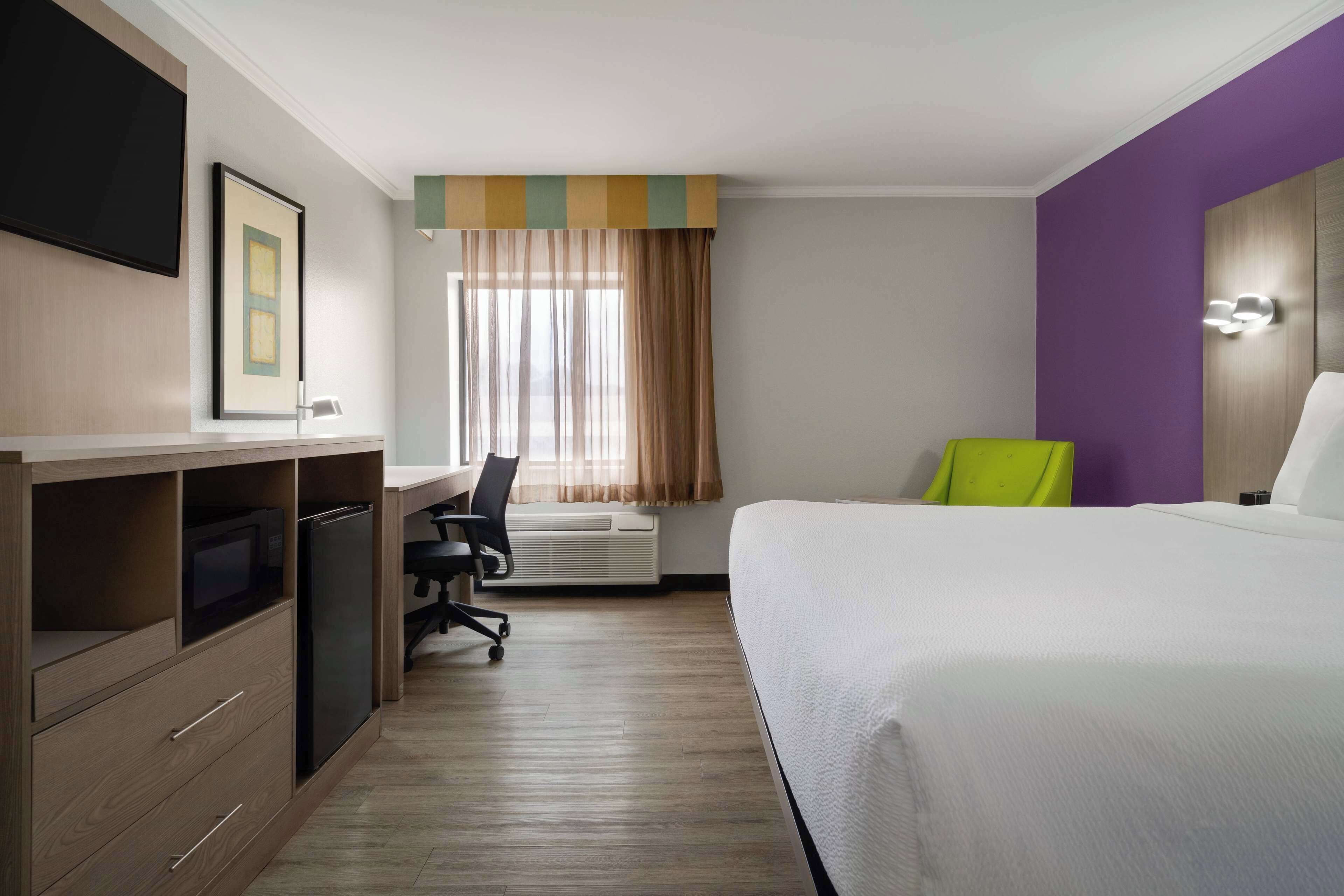 A hotel room with a bed, desk, chair, and a television on the wall.
