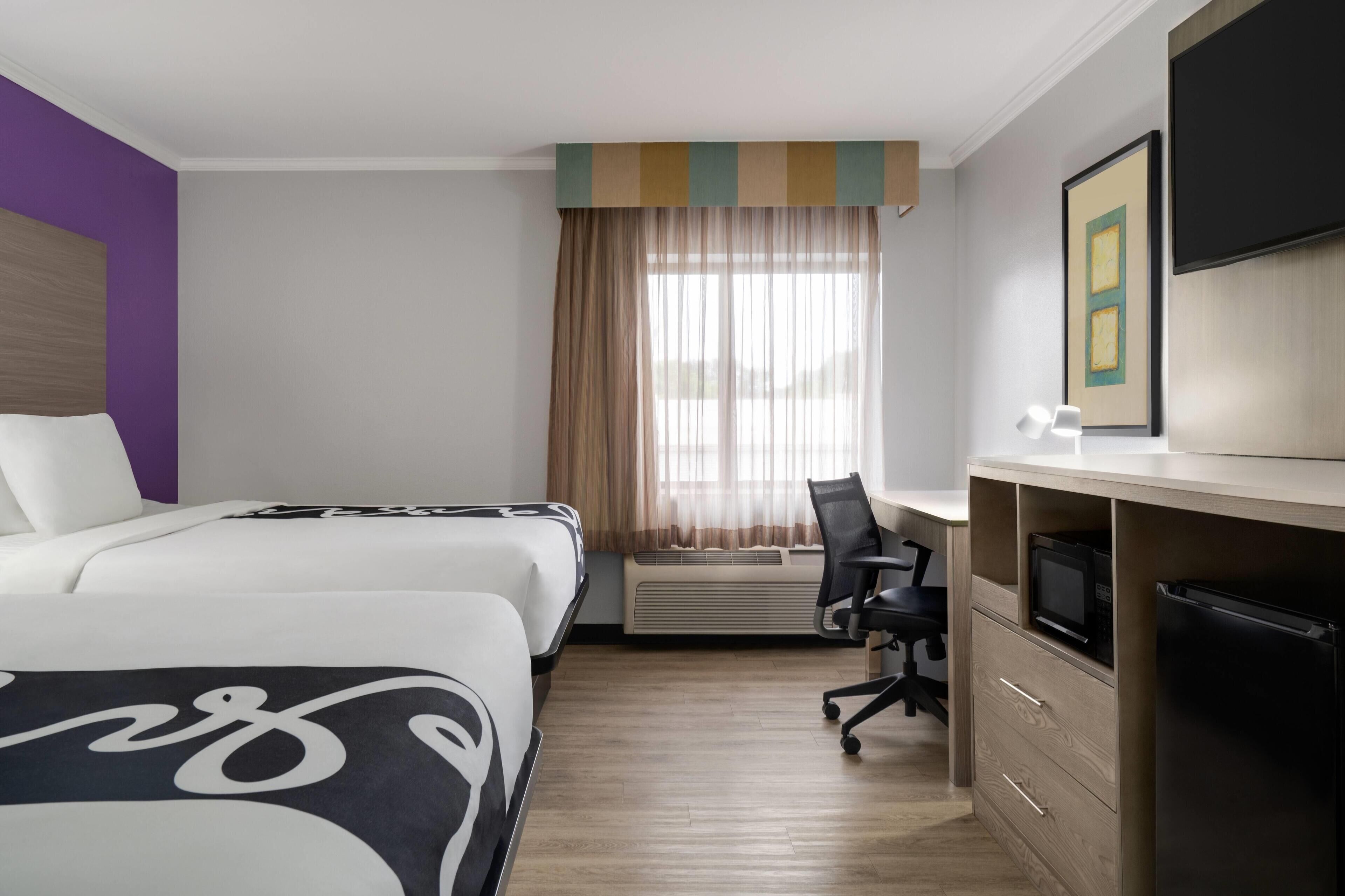 A hotel room with a bed, a desk with a chair, a TV, and a microwave.
