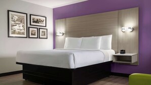 Una habitación de hotel moderna con una cama grande, un cabecero con iluminación integrada, una mesita de noche con lámpara y cuadros enmarcados en la pared.