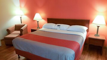 Una habitación de hotel con una cama grande, dos lámparas de noche, una silla y una mesita de noche.