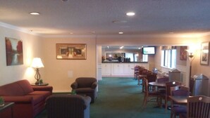 A hotel lobby with a red sofa, striped armchair, and dining area with wooden chairs and tables. - Motel 6 Maryland Heights, MO (Maryland Heights)