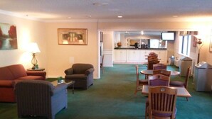 A living room with a sofa, armchair, and a dining area with chairs and a table. A kitchen is visible in the background. - Motel 6 Maryland Heights, MO (Maryland Heights)