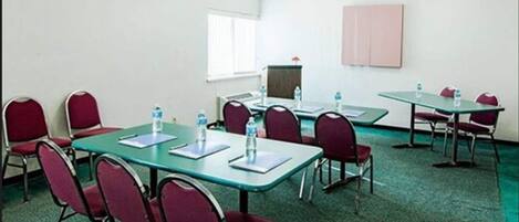 A conference room with tables and chairs, water bottles on tables, and a projector screen on the wall.