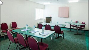 A conference room with green carpet, red chairs, and tables equipped with water bottles and notepads. - Motel 6 Maryland Heights, MO (Maryland Heights)