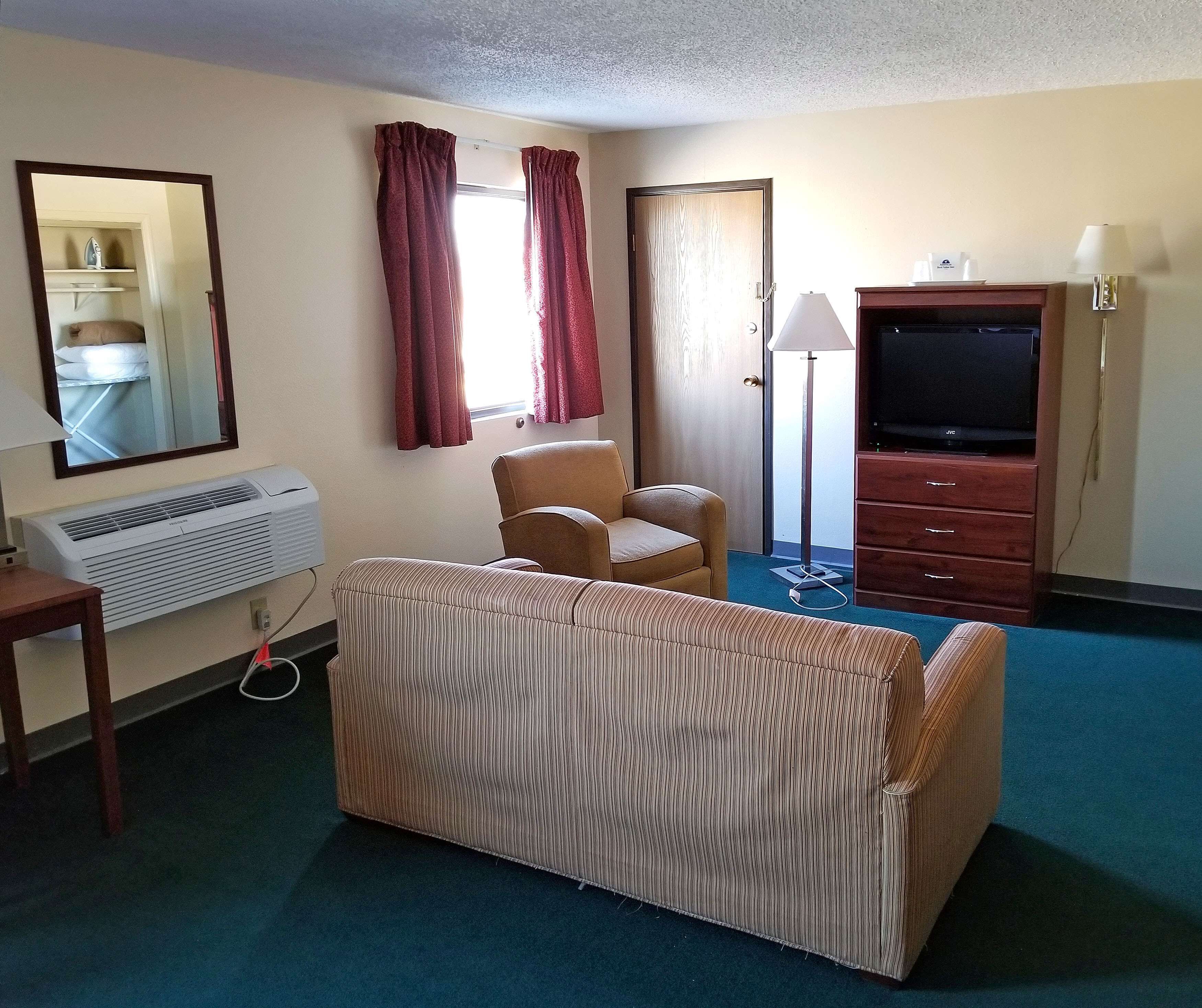 Een hotelkamer met een gestreepte bank, een televisie, een bureau met een lamp en een raam met gordijnen.