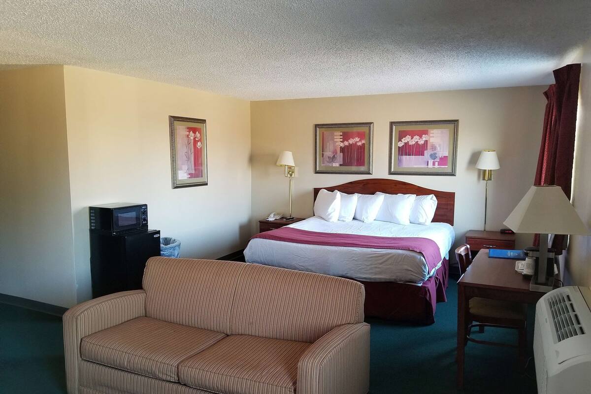 A hotel room with a bed, a sofa, a desk with a lamp, a telephone, and a microwave.