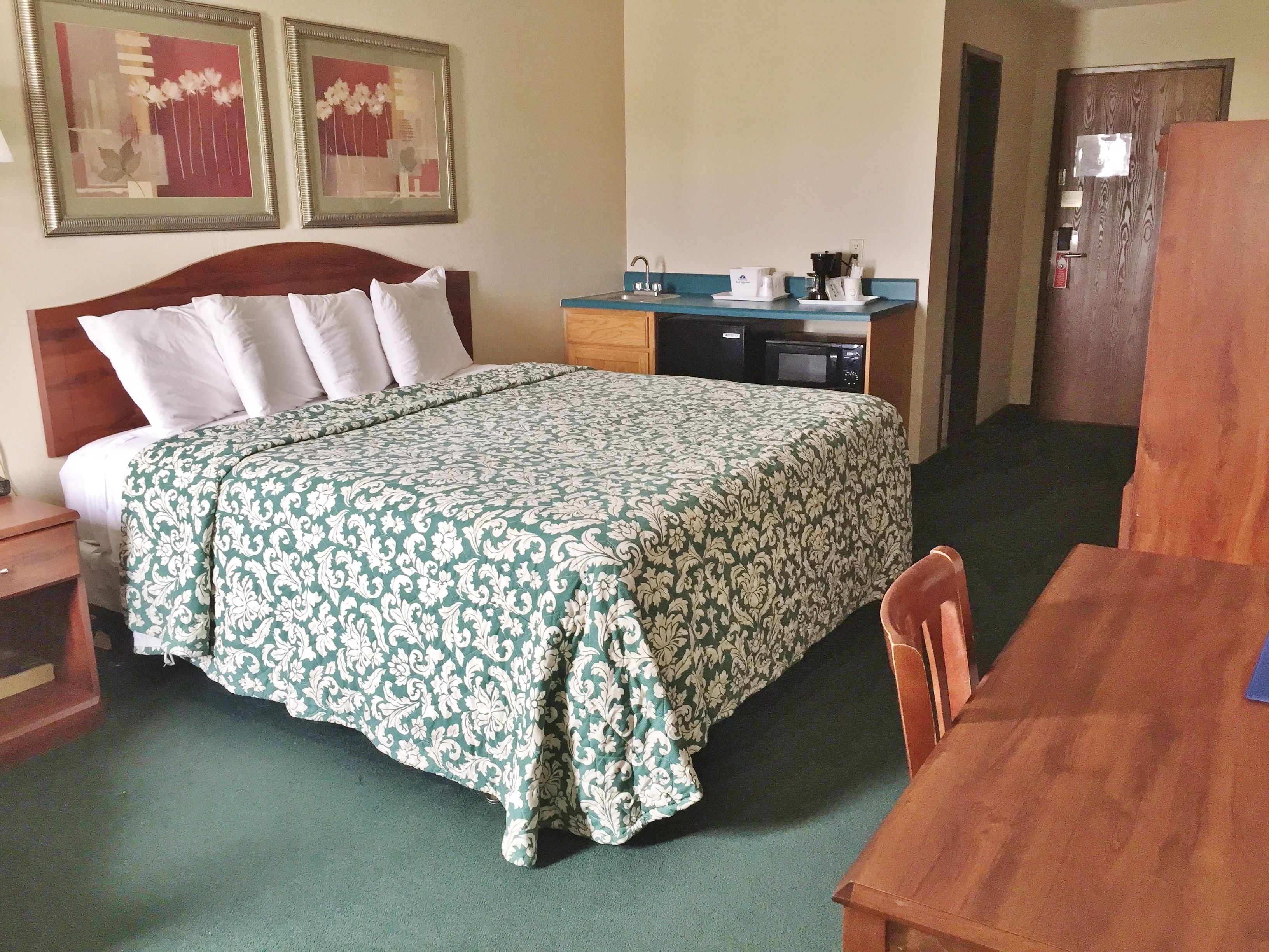 A hotel room with a bed, a desk, a chair, a microwave, and a sink.