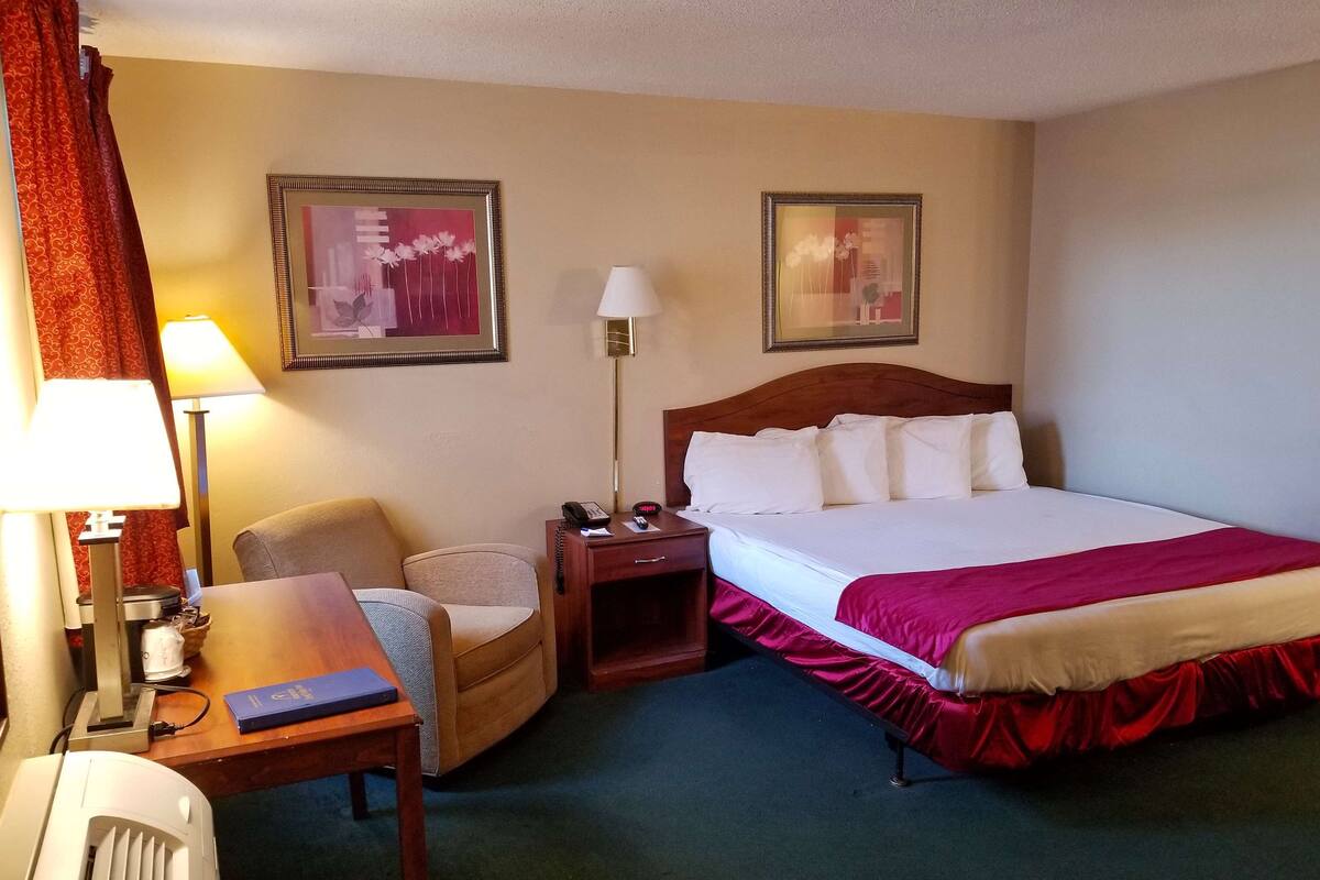 A hotel room with a bed, two bedside tables, a chair, a desk, a lamp, and two framed pictures on the wall.