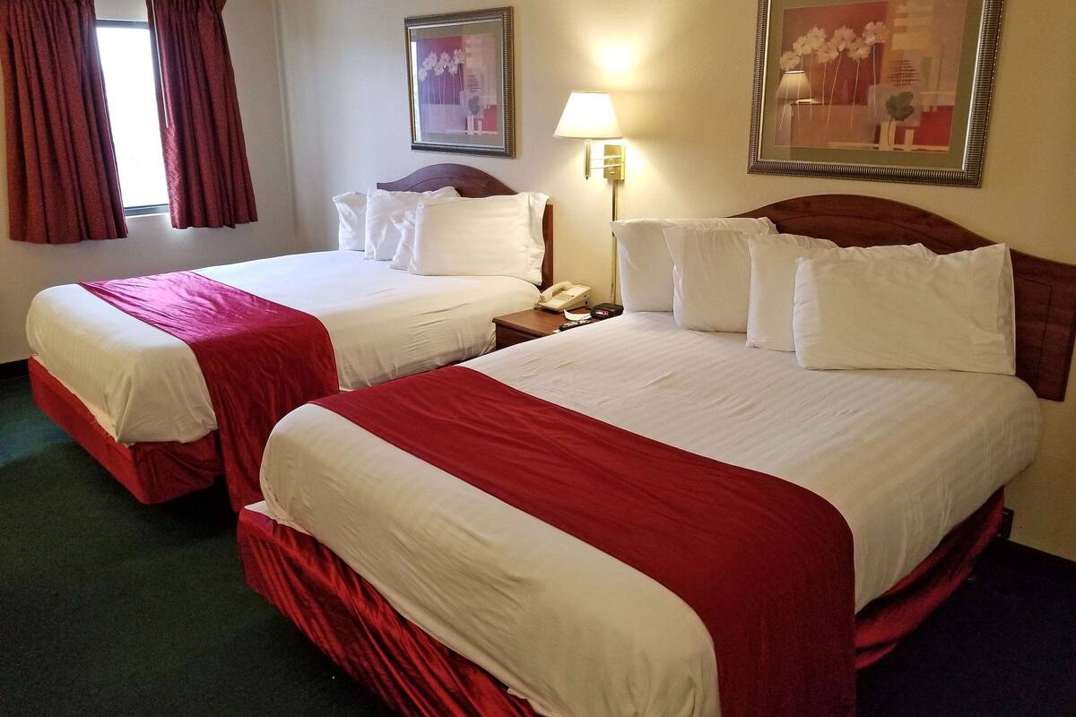 A hotel room with two beds, each with red and white bedding, a bedside lamp, and a framed picture on the wall.