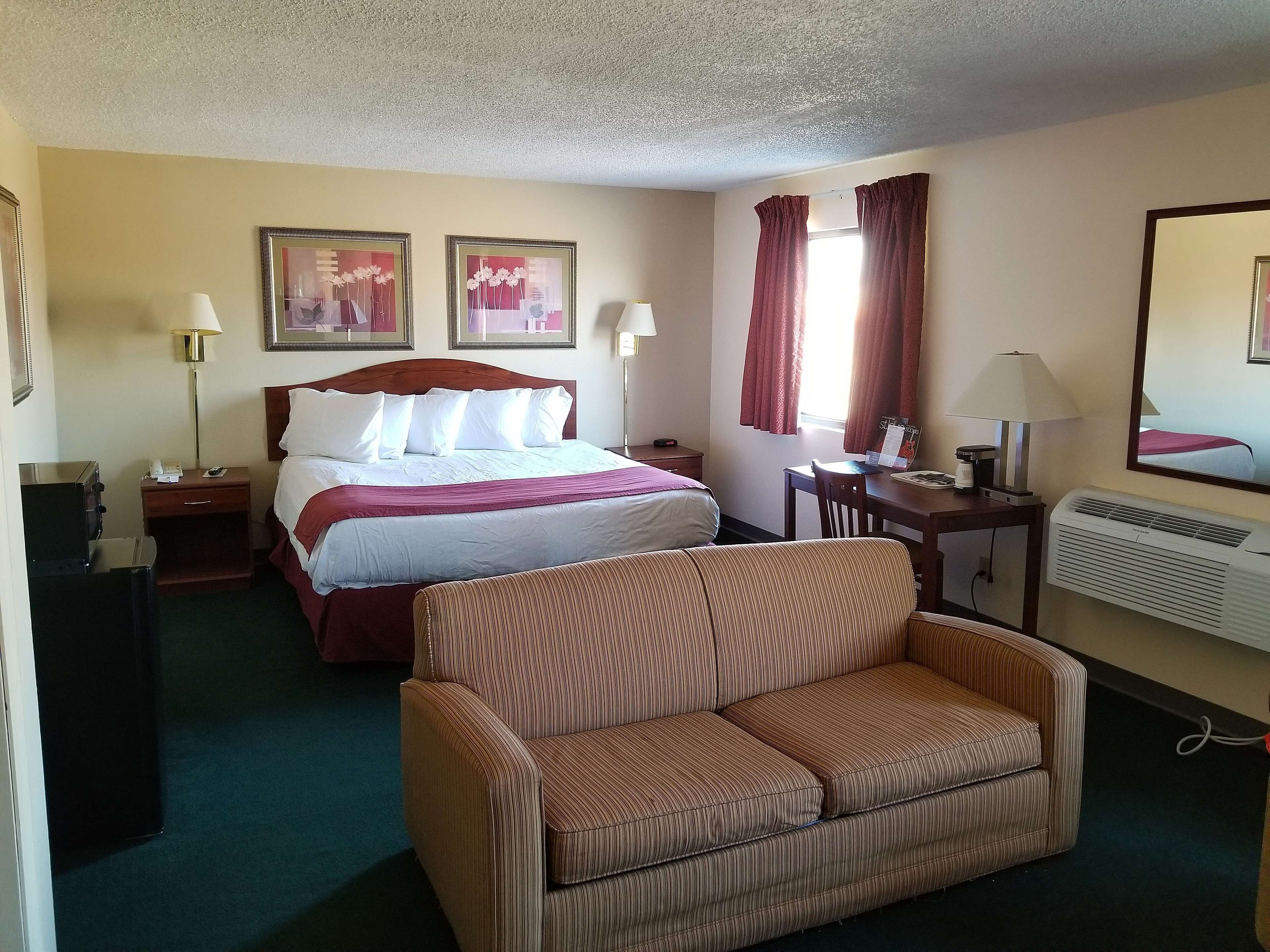 A hotel room with a bed, a desk, a chair, a sofa, and two paintings on the wall.