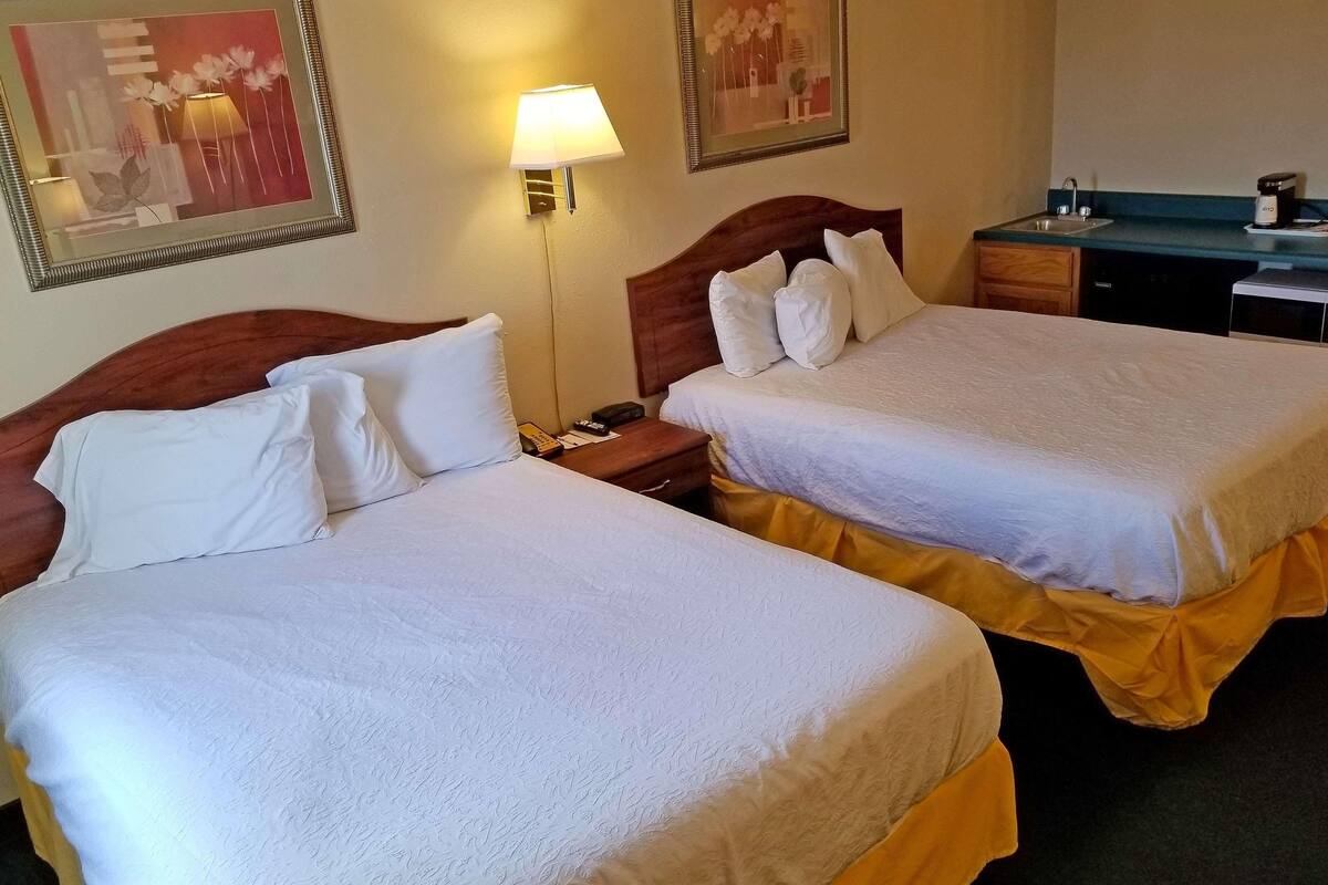 Two beds with white linens, a bedside lamp, a framed picture on the wall, and a coffee maker on the dresser.
