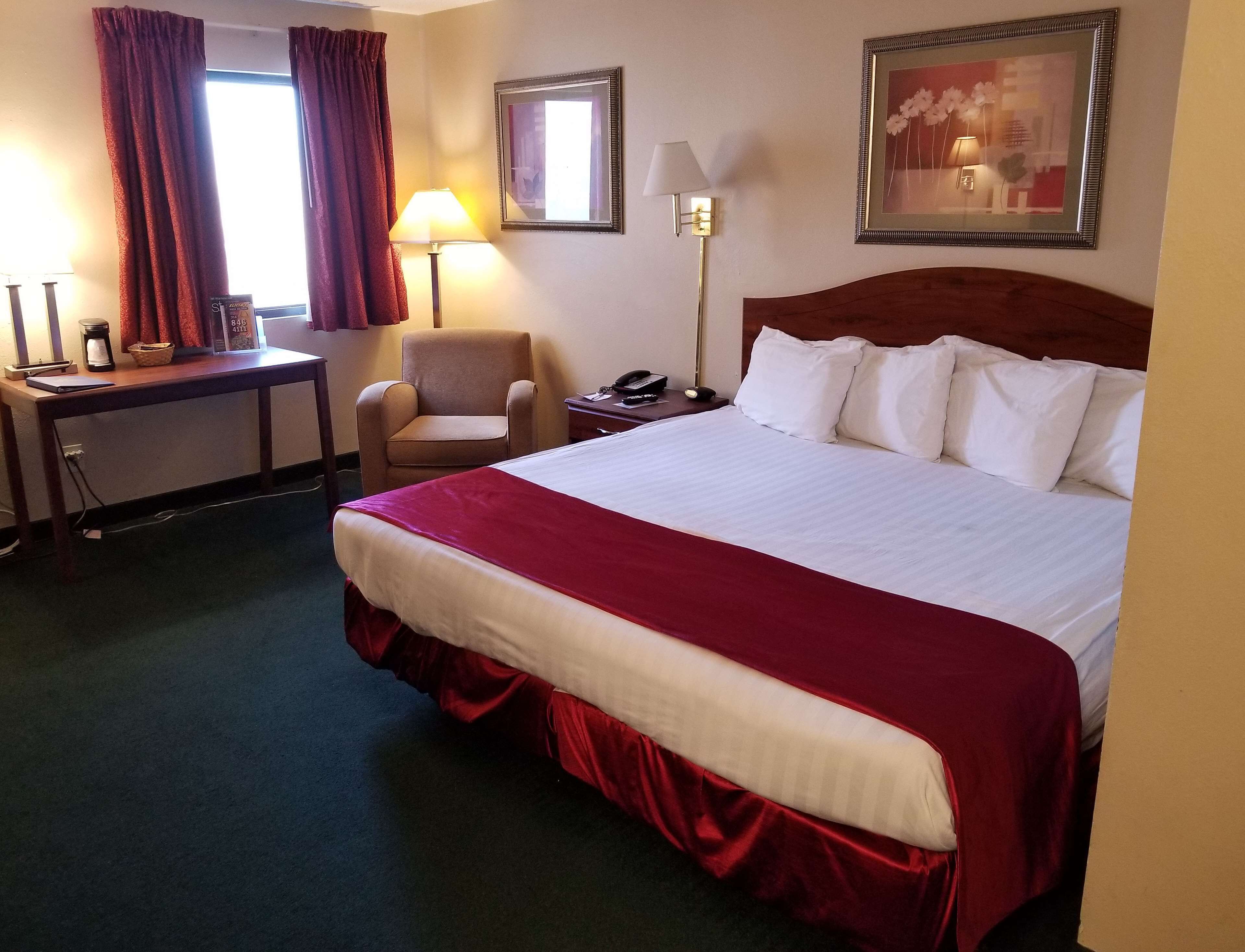 Ein Hotelzimmer mit einem großen Bett, einem Schreibtisch mit Lampe, einem Sessel und einem Nachttisch mit Telefon.