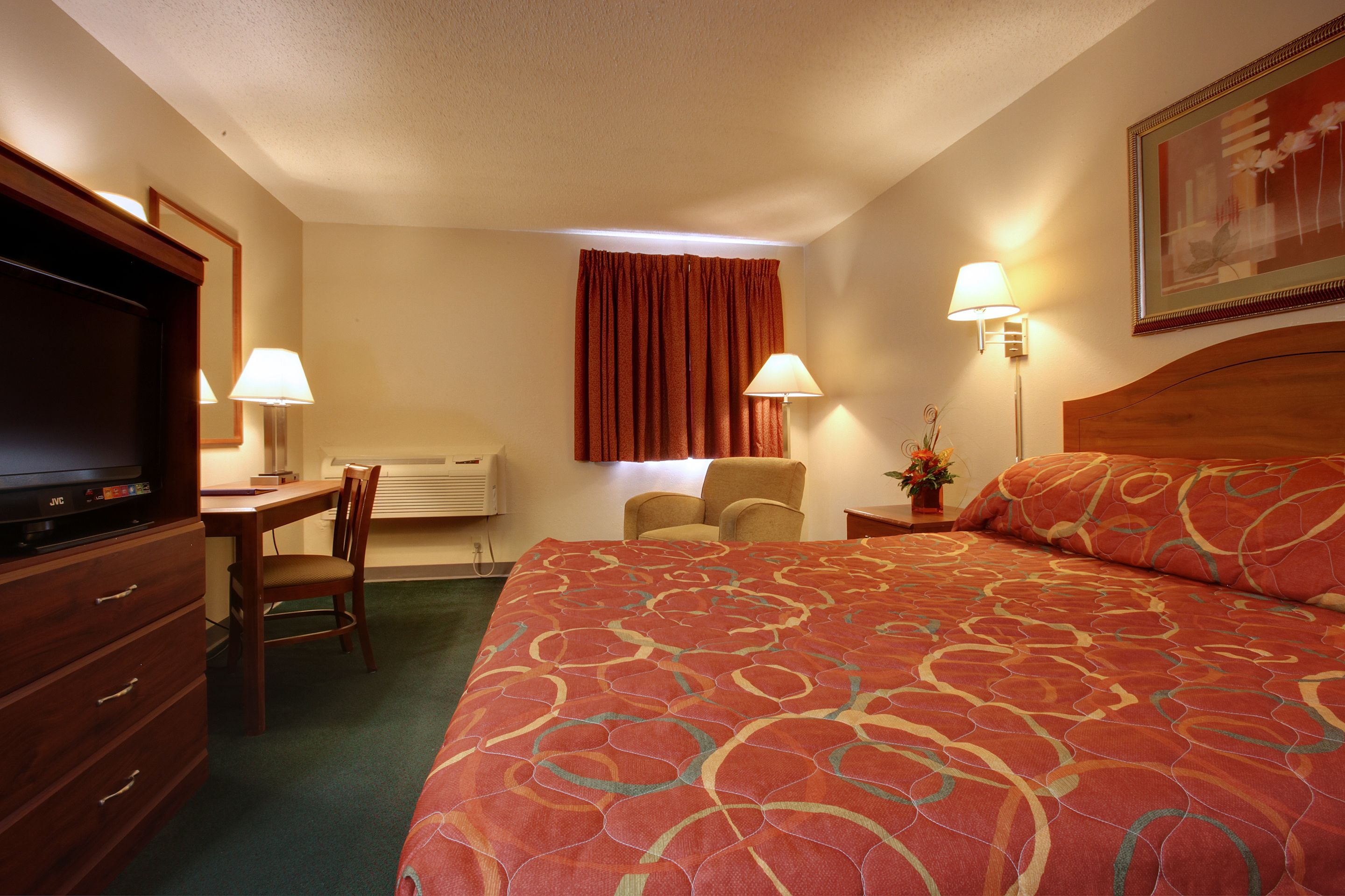 Ein Hotelzimmer mit einem großen Bett, einem Schreibtisch mit Stuhl, einem Fernseher und zwei Lampen.
