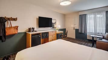 Habitación de hotel con cama, escritorio con lámpara, televisión, minibar, perchero y ventana con cortinas.