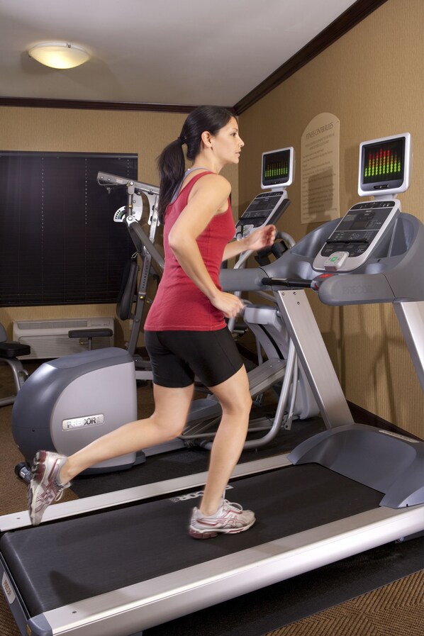 A woman running on a treadmill in a gym with exercise equipment and a wall with informational posters.