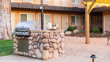 A stone barbecue grill with a built-in oven, a small table with a vase of flowers, and a pergola with string lights.