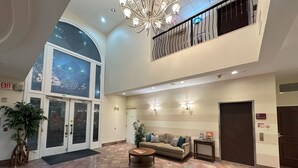 A spacious lobby with a high ceiling, a central seating area, and a staircase leading to an upper level.