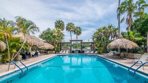 A swimming pool with lounge chairs and thatched umbrellas, surrounded by palm trees.