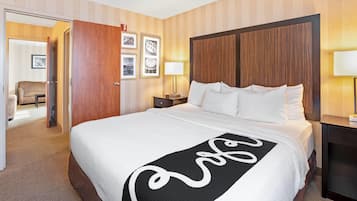 A hotel room with a large bed, wooden headboard, a bedside table with a lamp, and a door leading to a sitting area.