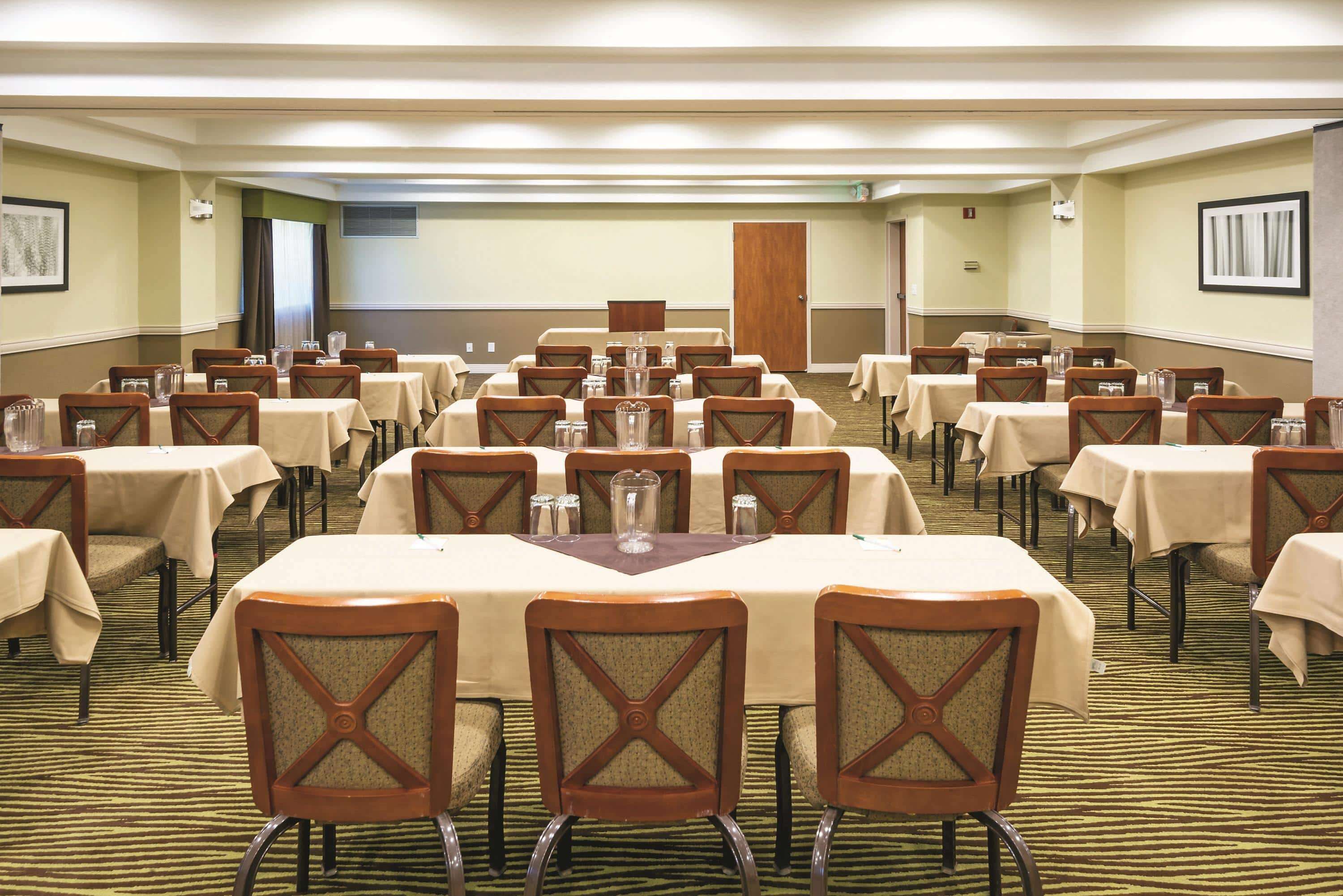A conference room with multiple tables and chairs, arranged in rows.