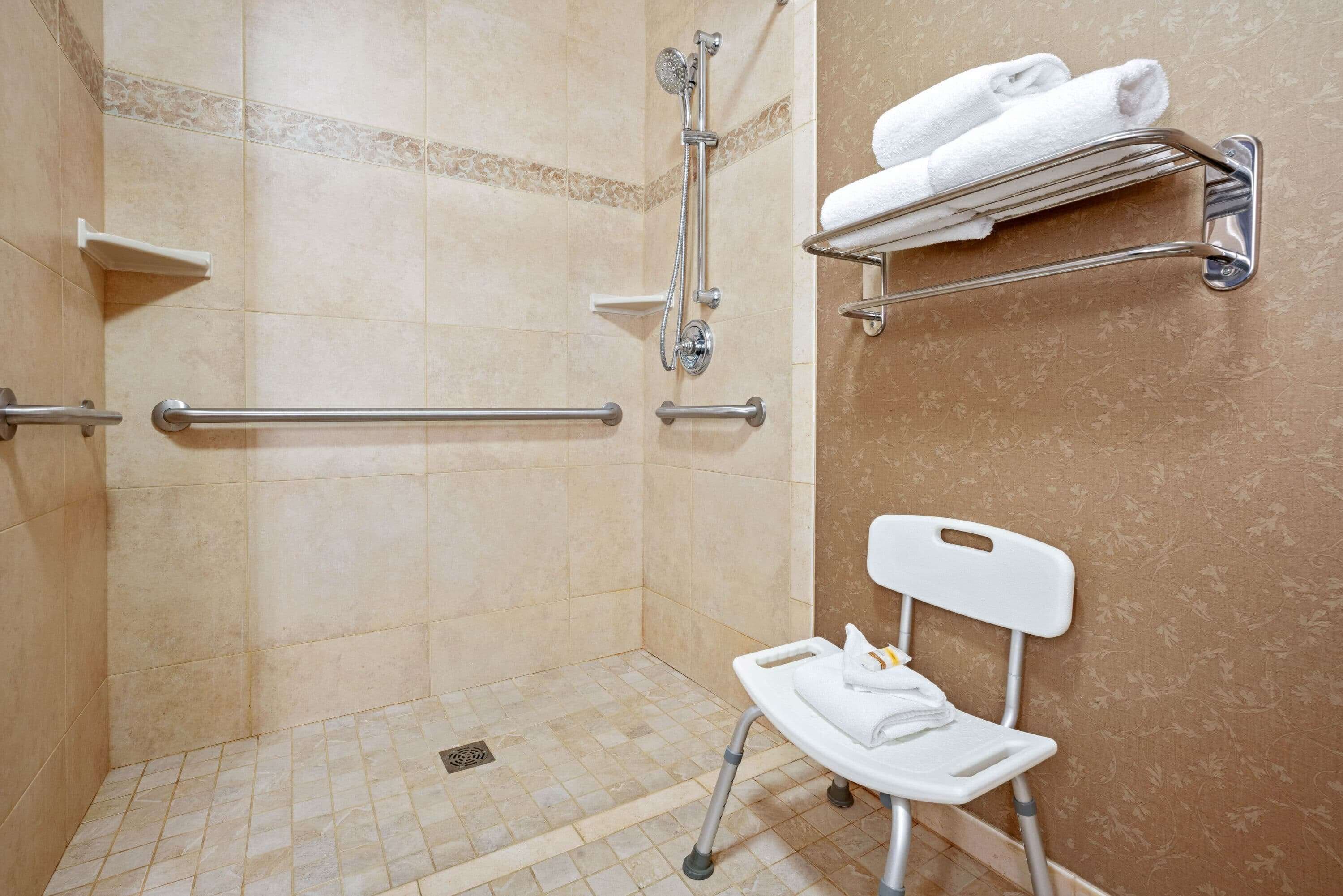 Un espace douche équipé de barres d’appui, une chaise blanche et un porte-serviettes avec des serviettes.