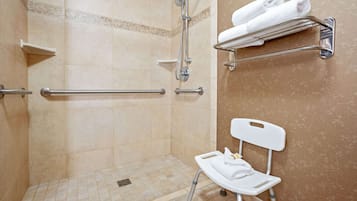A shower area with grab bars, a white chair, and a towel rack with towels.