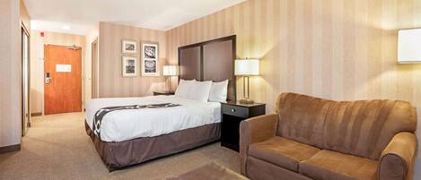 Una habitación de hotel con cama, sofá, mesita de noche y lámpara de pared.