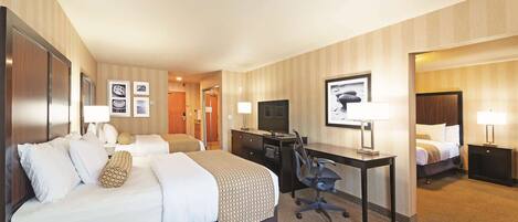 A hotel room with a large bed, a desk with a computer, a TV, and a separate bed.