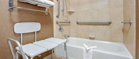 A bathroom with a white bathtub, grab bars, a white bench, and a towel rack.