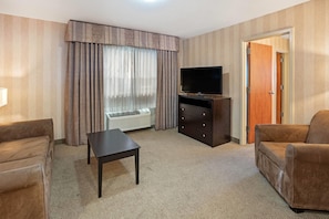 A hotel room with a sofa, a TV, a small table, and a door. - La Quinta Inn & Suites by Wyndham Boise Towne Square (Boise)