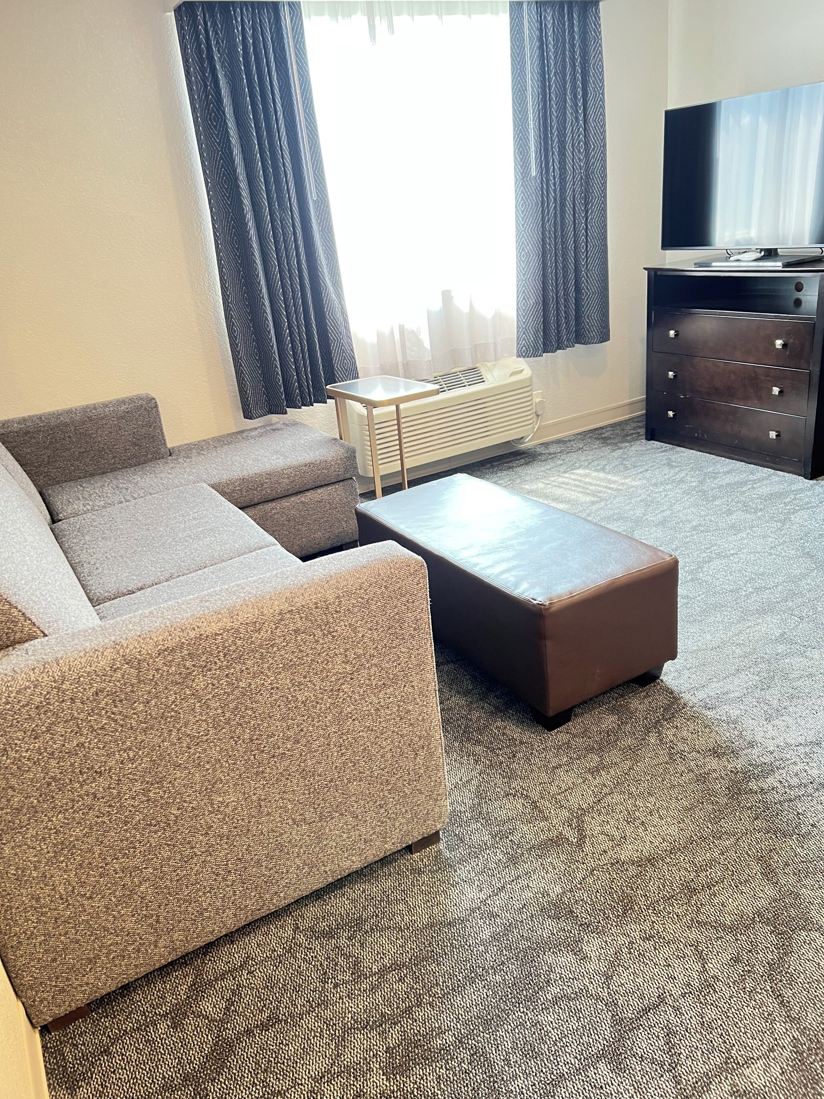 A living room with a sectional sofa, a coffee table, a TV, and a dresser.
