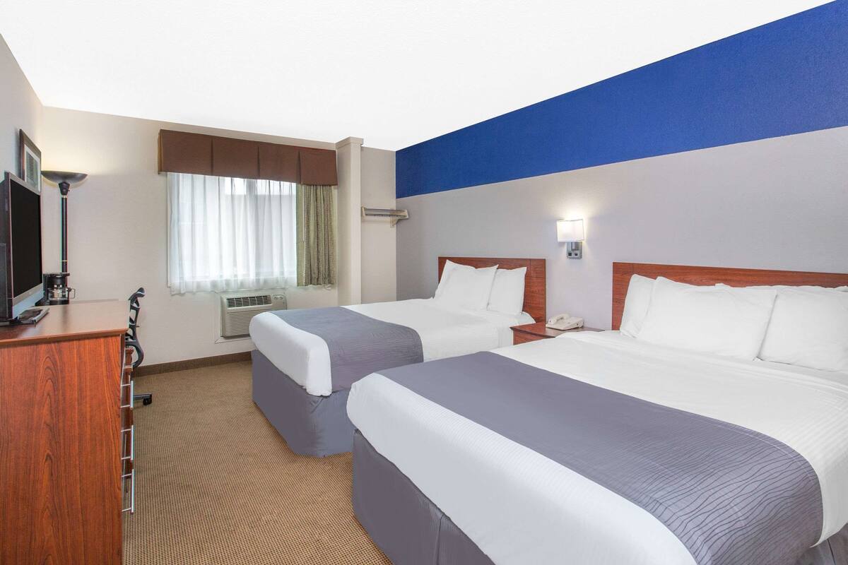 A hotel room with two beds, a desk, a television, and a window with curtains.