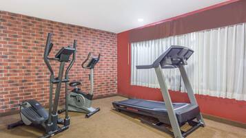 Une salle de sport avec un mur en briques, un tapis de course, un vélo elliptique et un vélo d’appartement.