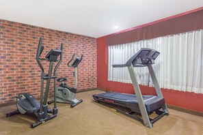 Ein Fitnessraum mit Backsteinwand, Laufband, Crosstrainer und Ergometer.