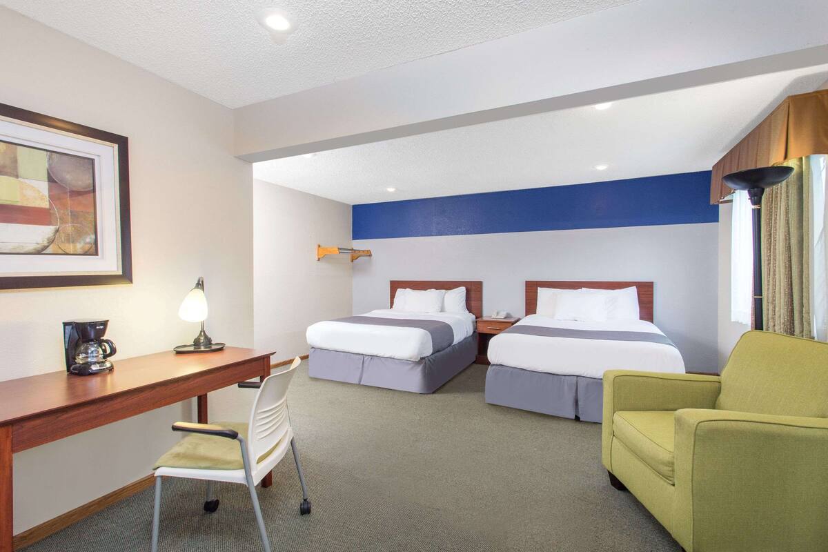 A hotel room with two beds, a desk, a chair, and a lamp.