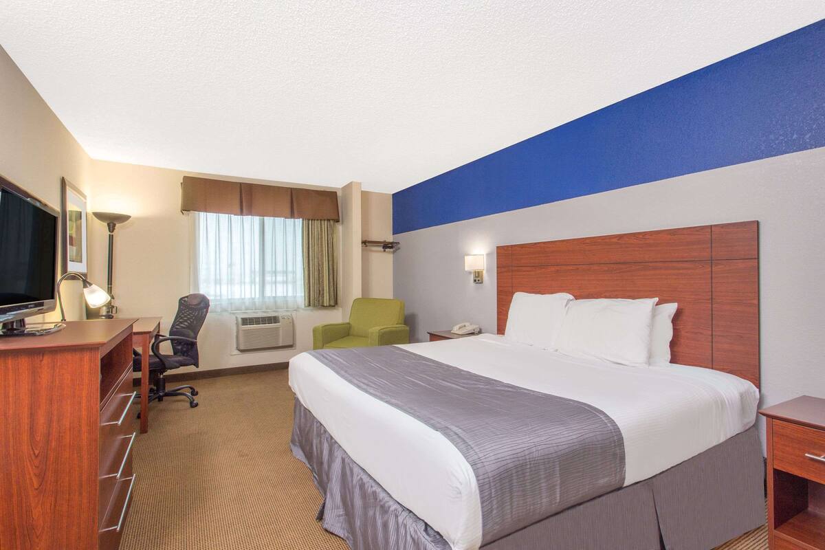 A hotel room with a large bed, a desk with a computer, a chair, a television, and a window with curtains.