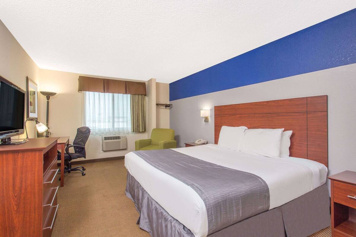 A hotel room with a bed, desk, chair, TV, and a window with curtains.