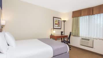 Habitación de hotel con una cama grande, un escritorio con silla, una lámpara, un cuadro en la pared y una ventana con cortinas.