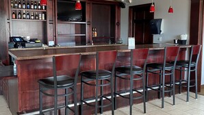 Eine Bar mit einer langen Theke, mehreren Hockern und einer Auswahl an Flaschen in Regalen.