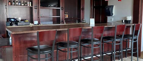 Una zona de bar con una barra alargada, varios taburetes y una variedad de botellas en estanterías.