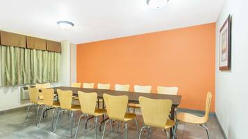 Een vergaderruimte met een lange tafel en meerdere stoelen, een raam met gordijnen en een oranje wand.