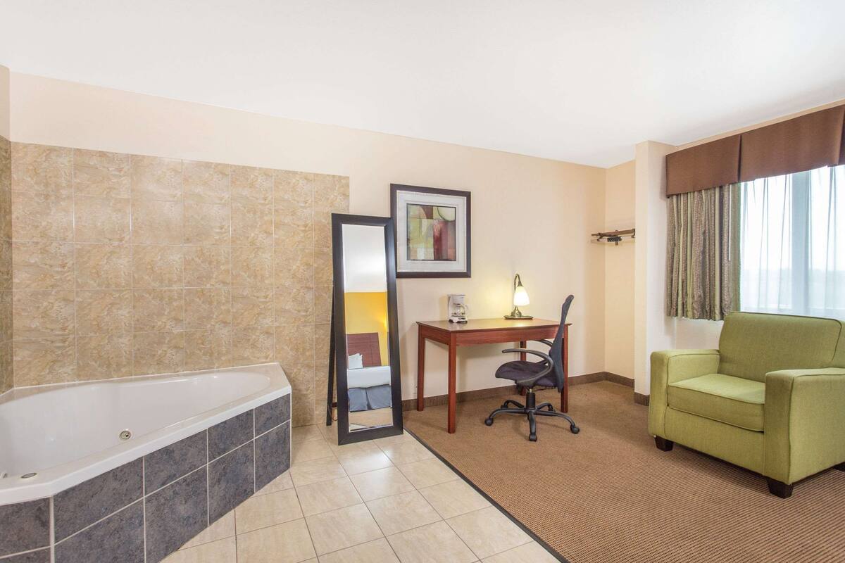 A hotel room with a bathtub, a desk with a chair, and a green sofa.