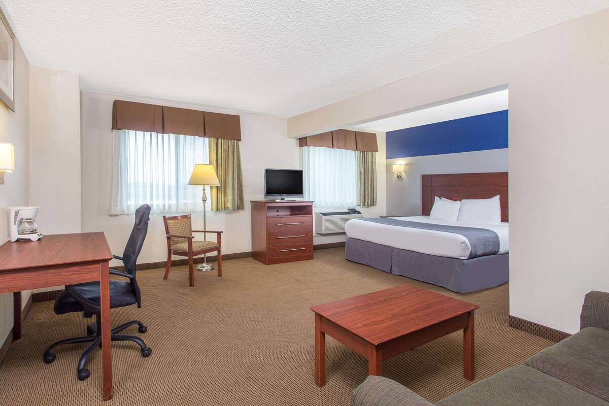 A hotel room with a bed, desk, chair, and a television.