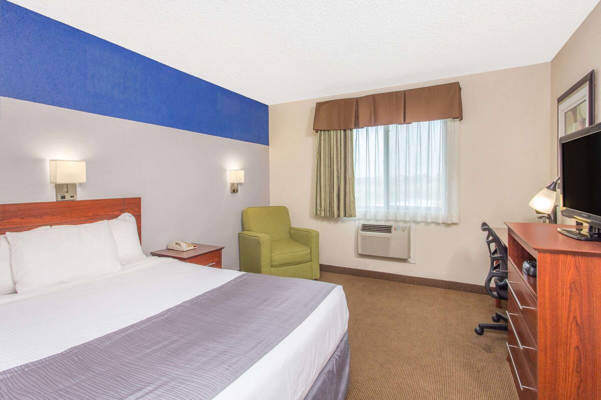 A hotel room with a large bed, a desk with a computer, a chair, and a television.
